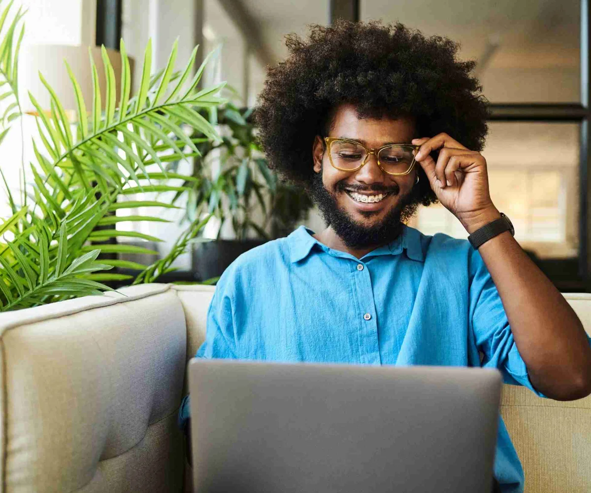 Man Smiling At His Laptop While Fixing Glasses